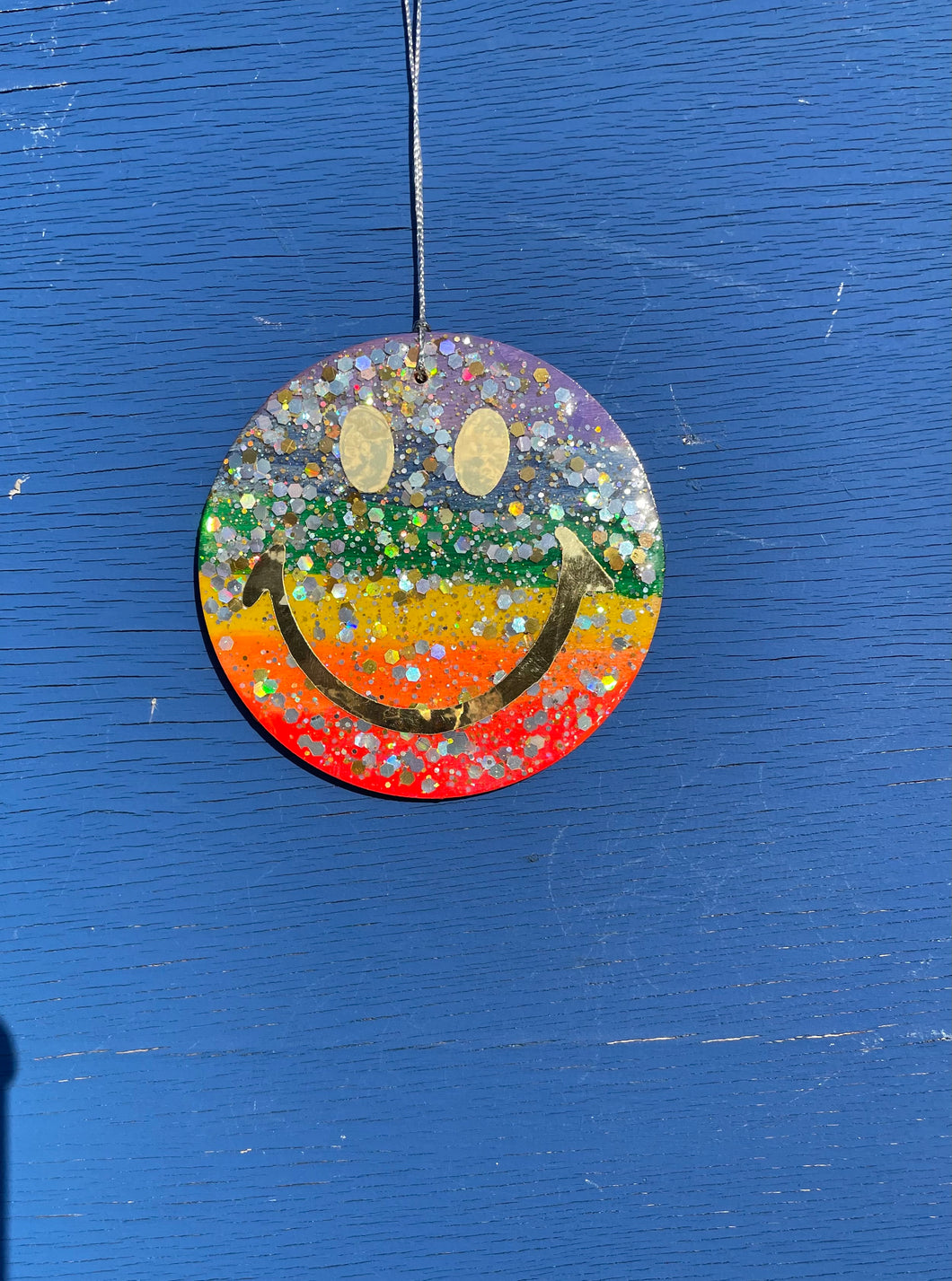 Rainbow glitter hanging smiley with gold eyes and mouth.